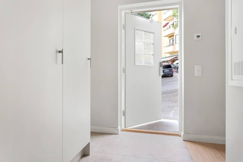 Hall med vita garderober och ekparkett, med en öppen dörr som leder ut till uteplatsen.