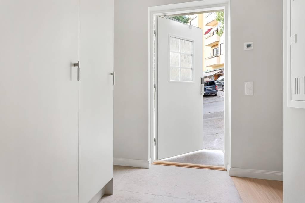 Hall med vita garderober och ekparkett, med en öppen dörr som leder ut till uteplatsen.