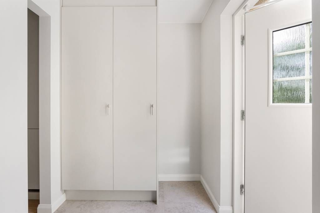 Ljus hall med platsbyggda vita garderober från golv till tak och infällda spotlights.