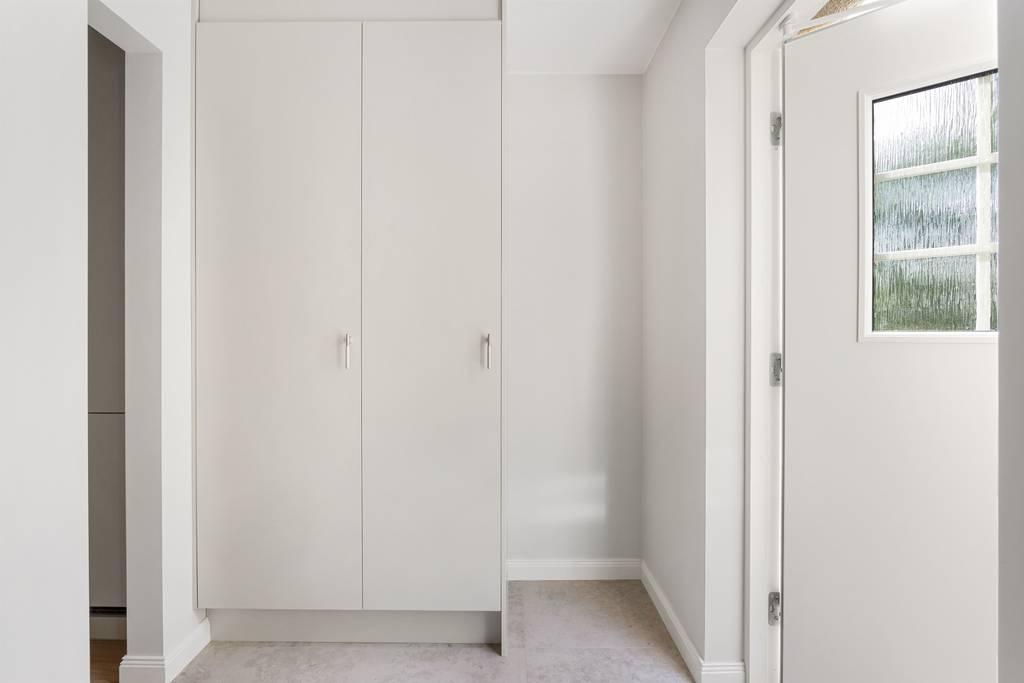 Ljus hall med platsbyggda vita garderober från golv till tak och infällda spotlights.