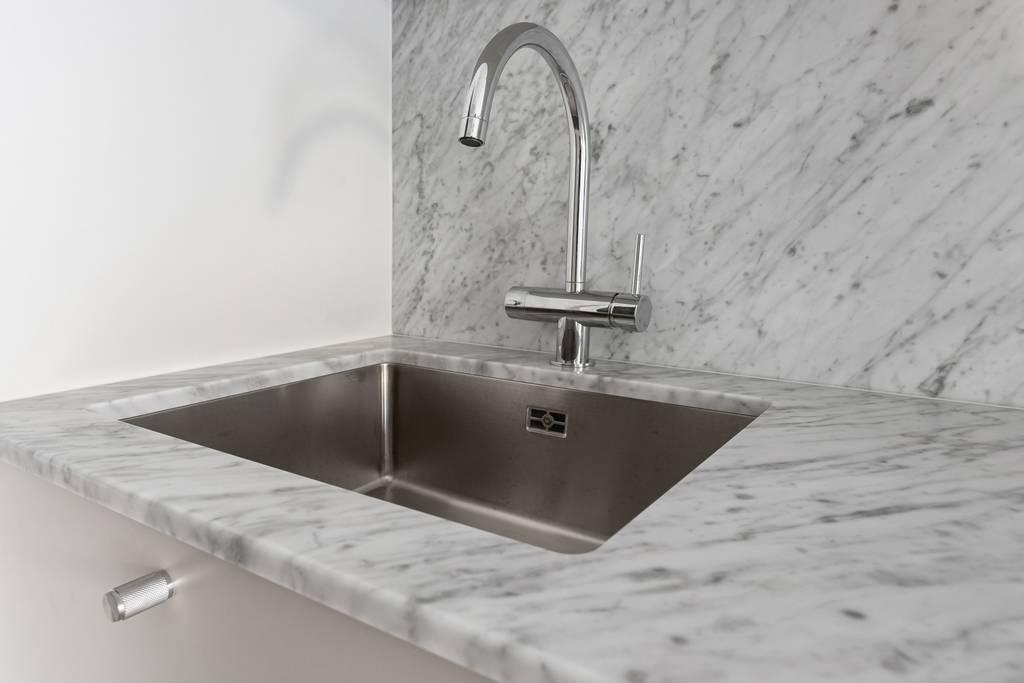 Närbild på den undermonterade diskon i rostfritt stål med modern blandare, infälld i en bänkskiva och stänkskydd av marmor.