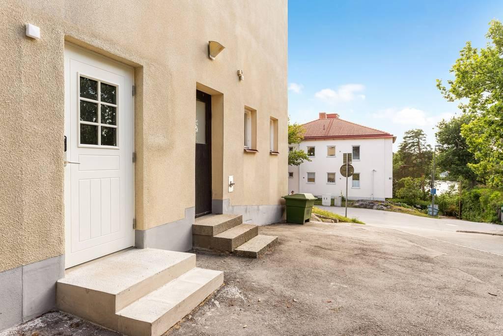 Exteriörbild som visar entrén till bostaden med en vit dörr och trappa i betong.