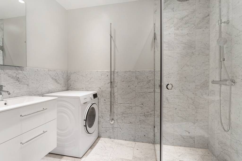 Del av det helkaklade badrummet som visar en tvättmaskin installerad bredvid duschhörnan.