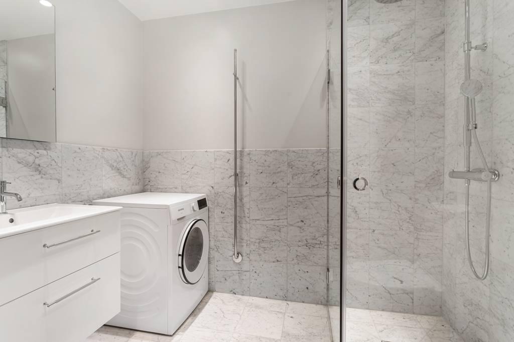 Del av det helkaklade badrummet som visar en tvättmaskin installerad bredvid duschhörnan.