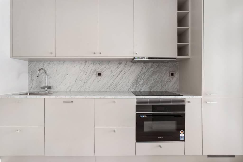 Kökets inredning med vita luckor, bänkskiva i marmor samt integrerad ugn och spishäll.