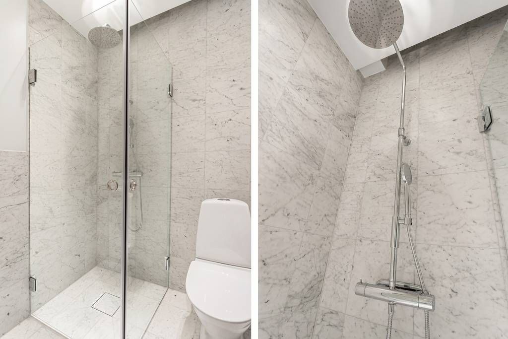 Det helkaklade badrummet med grå stenkeramik, sett från sidan, med toalett och duschhörna.